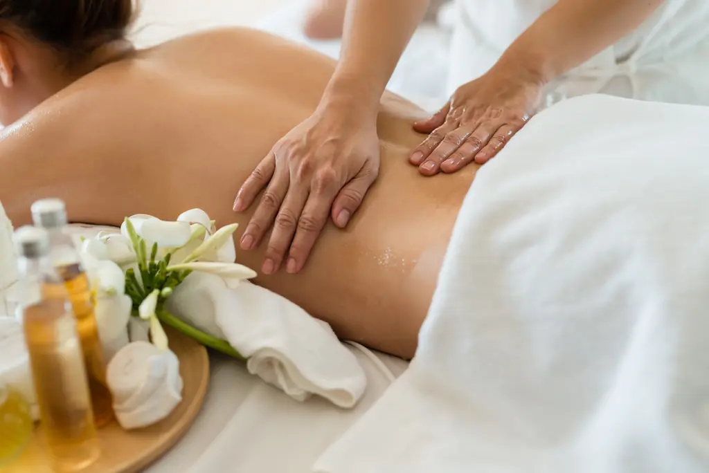A therapist massaging a client's lower back beside massage oils and white flowers