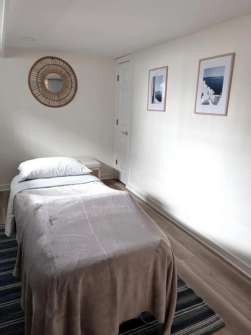 The Caldera Wellness treatment room: a massage table with soft blankets, a rattan mirror and framed seaside prints